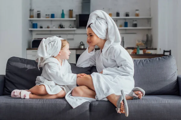 Ребенок и мама разговаривают, сидя на диване в халатах и полотенцах на головах — стоковое фото