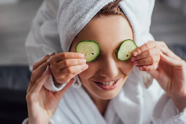 Vista recortada del niño aplicando rodajas de pepino fresco en los ojos de la madre, enfoque selectivo - foto de stock