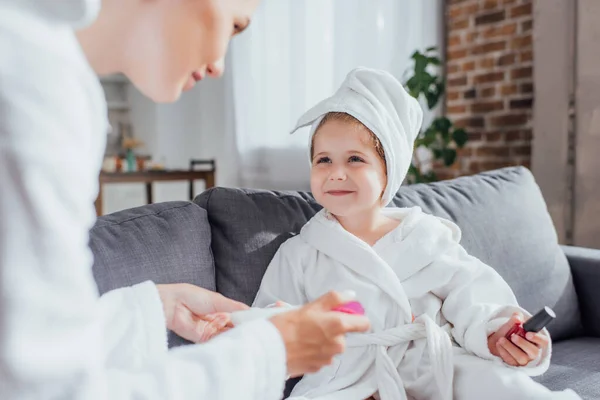 Селективное внимание женщины, делающей маникюр ребенку в белом халате и полотенце на голове — стоковое фото