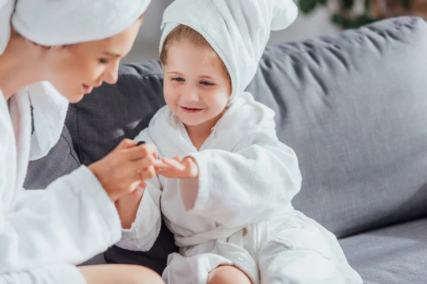 Selective focus of young mother making manicure to daughter in white bathrobe and towel on head — Stock Photo