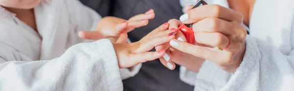 Ausgeschnittene Ansicht einer Frau, die Fingernägel ihrer Tochter mit rotem Lack bedeckt, horizontales Bild — Stockfoto