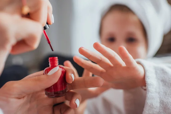 Vista recortada de la mujer que aplica esmalte rojo en las uñas de la hija, enfoque selectivo - foto de stock