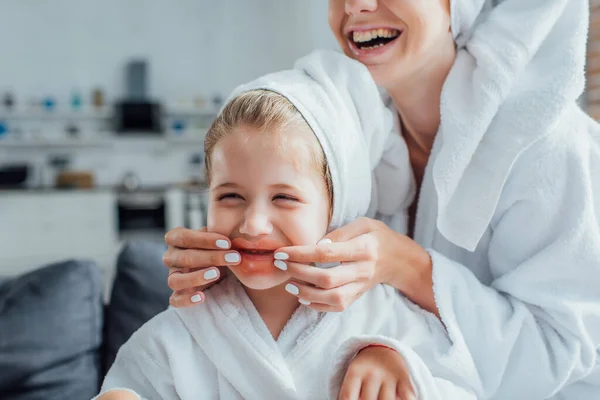 Vista parziale della donna che applica il cerotto all'idrogel sulle labbra della figlia in asciugamano bianco sulla testa — Foto stock