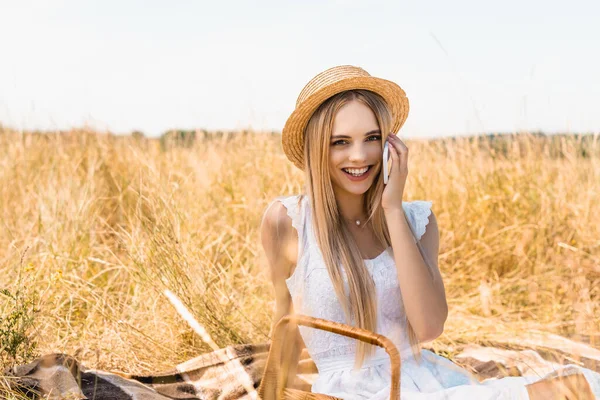 Foco seletivo de mulher loira elegante em roupa de verão falando no smartphone enquanto olha para a câmera em campo — Fotografia de Stock