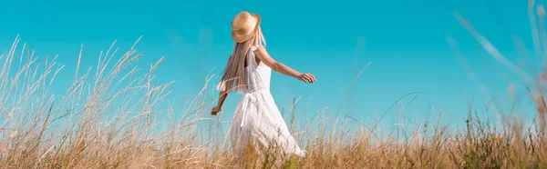 Encabezado del sitio web de la mujer en vestido blanco y sombrero de paja de pie con las manos extendidas en el campo contra el cielo azul - foto de stock