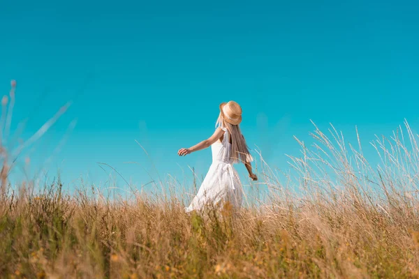 Selective focus of woman in straw hat and white dress standing with outstretched hands on grassy field — Stock Photo