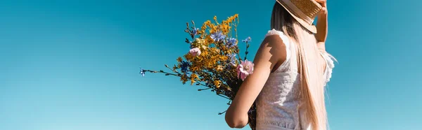 Jovem mulher em roupa de verão segurando buquê de flores silvestres contra o céu azul, imagem horizontal — Fotografia de Stock