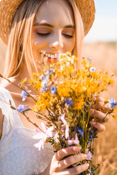 Selective focus of sensual woman in straw hat holding bouquet of wildflowers in sunshine — Stock Photo