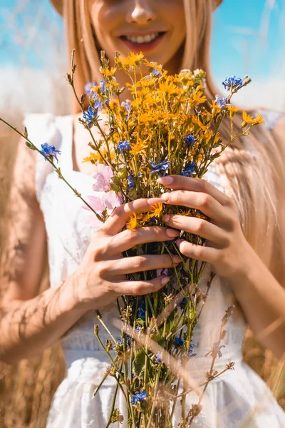 Vista parcial de mujer joven sosteniendo ramo de flores silvestres, enfoque selectivo - foto de stock