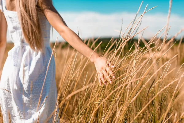 Cropped view of woman in white dress touching spikelets while standing in grassy field — Stock Photo