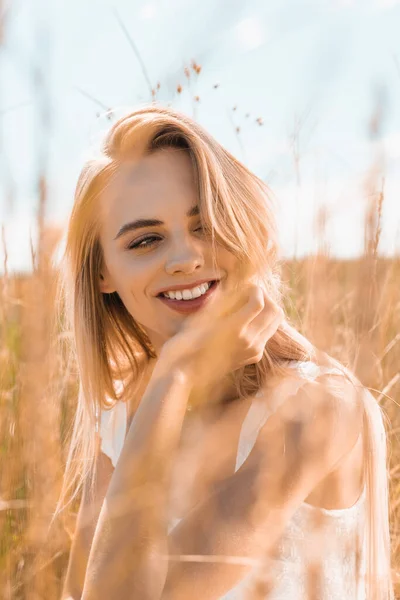 Selektiver Fokus einer jungen blonden Frau, die die Hand in der Nähe des Gesichts hält, während sie im Grasland wegschaut — Stockfoto