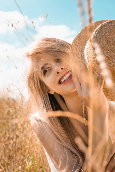 Selective focus of sensual blonde woman holding straw hat while looking away in grass — Stock Photo