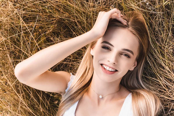 Vista dall'alto della donna bionda eccitata che tocca la testa mentre giace sull'erba e guarda la fotocamera — Foto stock