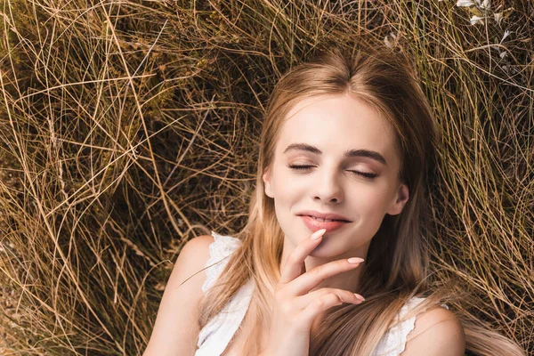 Vista superior da mulher loira sensual tocando lábios enquanto deitado na grama verde com olhos fechados — Fotografia de Stock