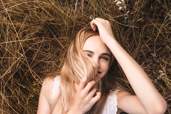 Вид зверху молода блондинка лежить на траві і дивиться на камеру під час затемнення обличчя з волоссям — стокове фото