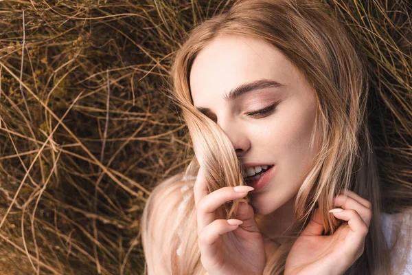 Vue de dessus de la femme blonde sensuelle couchée sur l'herbe verte avec les yeux fermés et le visage obscurcissant avec les cheveux — Photo de stock