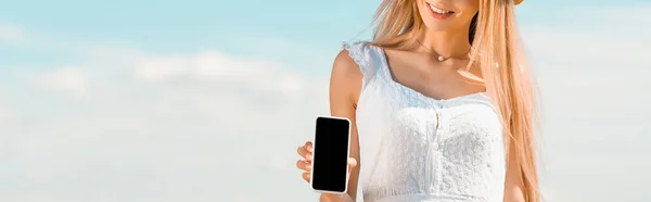 Teilansicht der blonden Frau zeigt Smartphone mit leerem Bildschirm vor blauem Himmel, Website-Header — Stock Photo