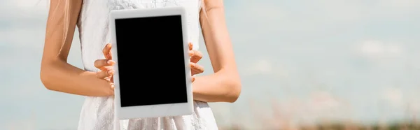 Обрезанный вид женщины, показывающей цифровой планшет с чистым экраном на фоне голубого неба, горизонтальное изображение — стоковое фото