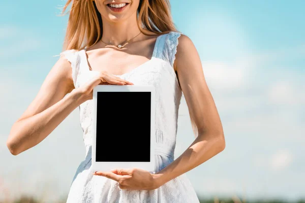 Ausgeschnittene Ansicht einer jungen Frau im weißen Kleid, die ein digitales Tablet mit leerem Bildschirm vor blauem Himmel zeigt — Stockfoto
