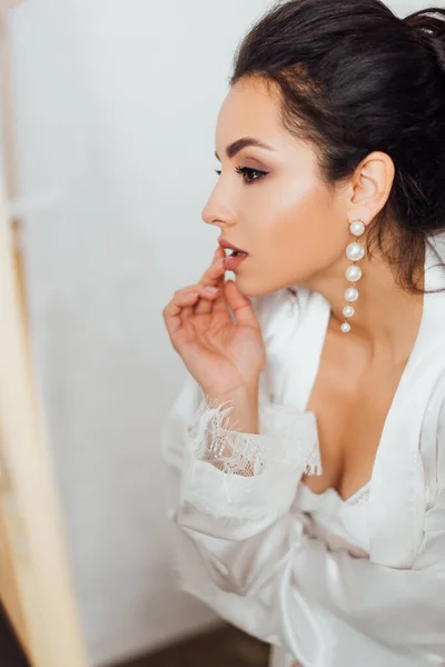 Morena novia en túnica de seda y sujetador tocando los labios y mirando hacia otro lado — Stock Photo