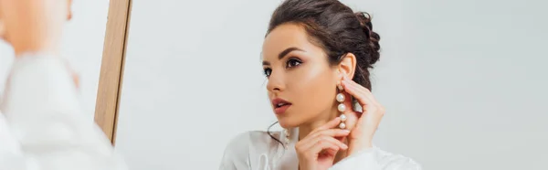 Panoramic shot of bride in silk robe putting on pearl earring near mirror — Stock Photo