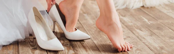 Panoramic crop of bride putting on white heels at home — Stock Photo