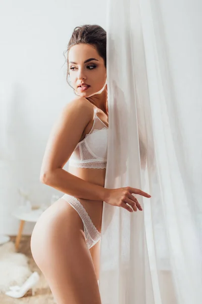 Sexy bride in lace underwear looking away near curtains at home — Stock Photo