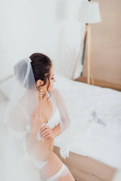 Вибірковий фокус брюнетки нареченої в нижній білизні, підв'язці і вуаль, стоячи в спальні — стокове фото