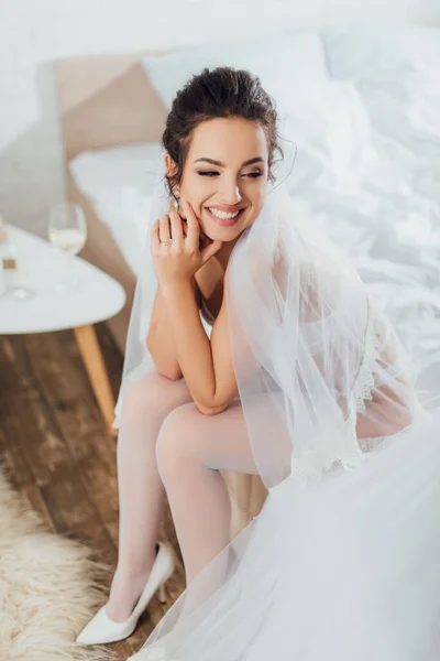Невеста в нижнем белье, вуаль и чулки глядя в сторону свадебного платья на кровать — стоковое фото