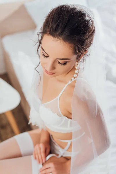 Concentration sélective de la mariée en boucle d'oreille perle et lingerie toucher bas sur le lit — Photo de stock