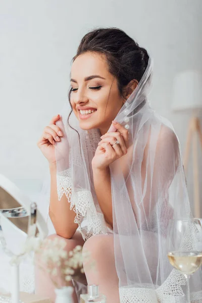 Selective focus of bride in veil sitting near mirror and glass of wine — Stock Photo