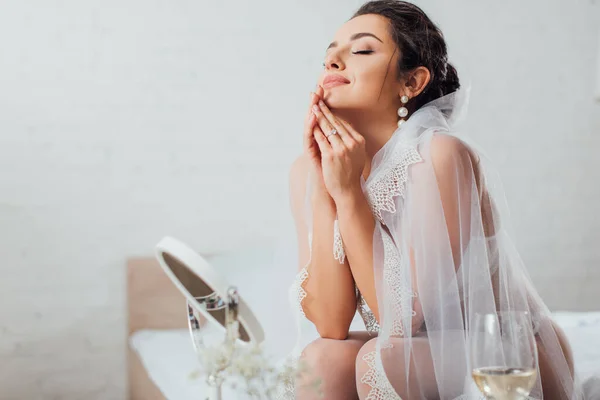Selektiver Fokus der Braut in Dessous und Schleier, die neben Glas Wein und Spiegel auf dem Bett sitzt — Stockfoto