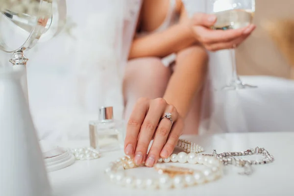 Vista recortada de la novia tocando collar de perlas y sosteniendo copa de vino en casa - foto de stock