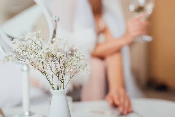 Selective focus of flowers in vase and bride holding glass of wine at background — Stock Photo