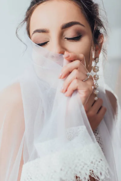 Selective focus of young bride in pearl earring touching lace veil — Stock Photo