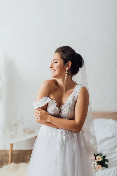 Novia joven en velo con los ojos cerrados usando vestido de novia en el dormitorio - foto de stock