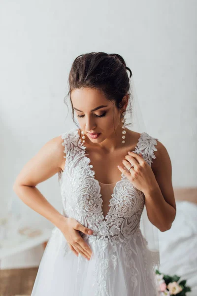 Selective focus of brunette bride touching lace wedding dress at home — Stock Photo