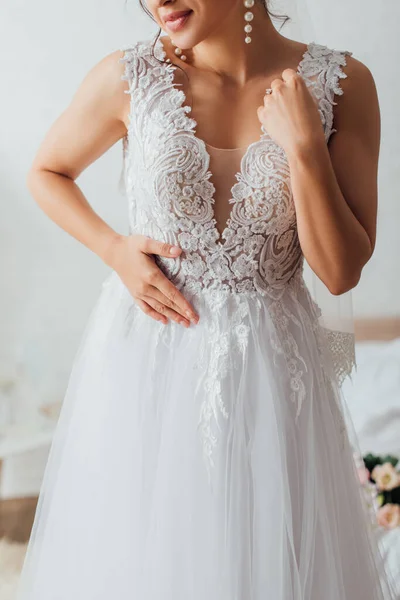 Cropped view of bride in pearl earrings touching wedding dress — Stock Photo