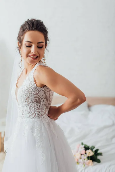 Jovem noiva em véu colocando em vestido de noiva em casa — Fotografia de Stock