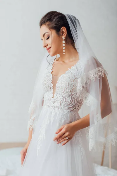 Junge Braut in Perlenohrringen, Schleier und Brautkleid zu Hause — Stockfoto