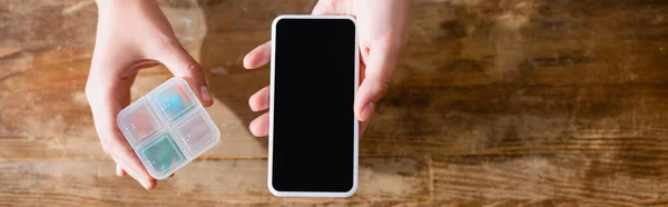 Panoramic crop of woman holding smartphone with blank screen and medication in pill organizer — Stock Photo