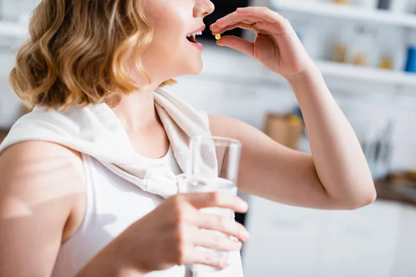 Vista ritagliata di giovane donna prendendo pillola e tenendo bicchiere d'acqua — Foto stock