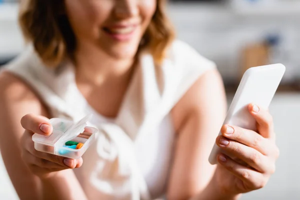 Selective focus of woman holding pill organizer and smartphone — Stock Photo