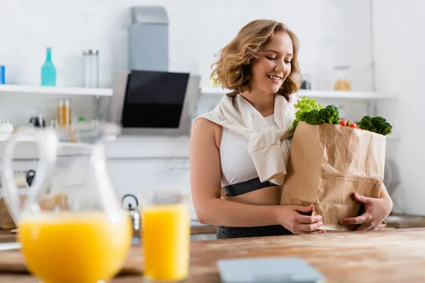 Enfoque selectivo de la mujer joven mirando bolsa de papel con comestibles - foto de stock