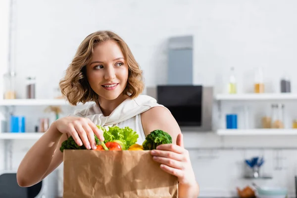 Young woman touching groceries in paper bag and looking away — Stock Photo