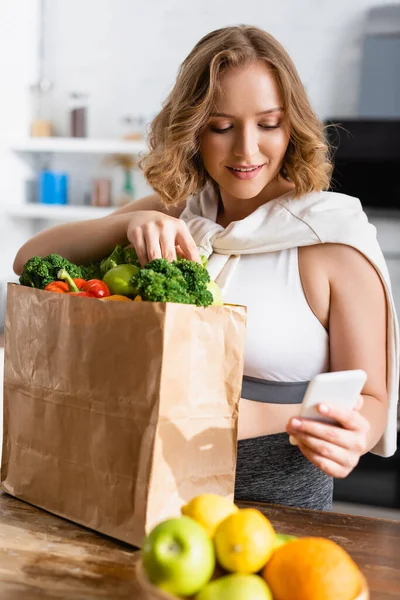 Selective focus of woman taking selfie with groceries in paper bag — Stock Photo