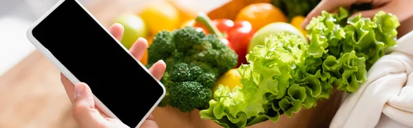 Панорамный урожай женщины, держащей смартфон с чистым экраном рядом с продуктами — стоковое фото