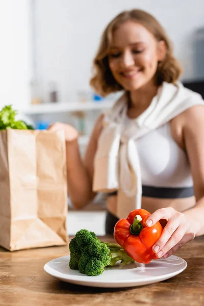Selective focus of woman putting bell pepper on plate near broccoli — Stock Photo