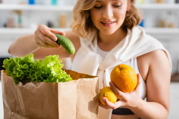 Selective focus of woman holding cucumber, lemon and orange near paper bag — Stock Photo