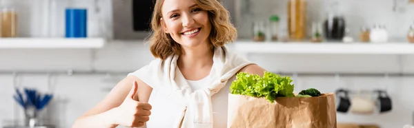 Panoramic crop of woman showing thumb up near paper bag with lettuce — Stock Photo